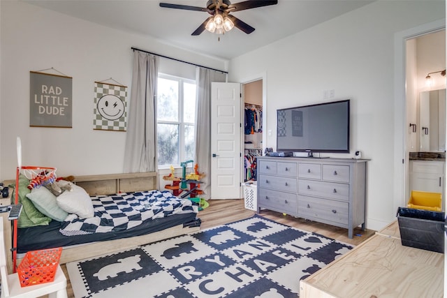 bedroom with a closet, light wood-style flooring, a walk in closet, and a ceiling fan