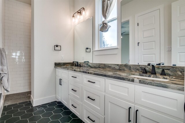 full bathroom featuring baseboards, tiled shower, double vanity, a sink, and tile patterned flooring