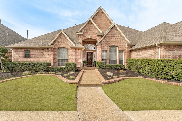 view of front of home featuring brick siding, a front yard, and roof with shingles