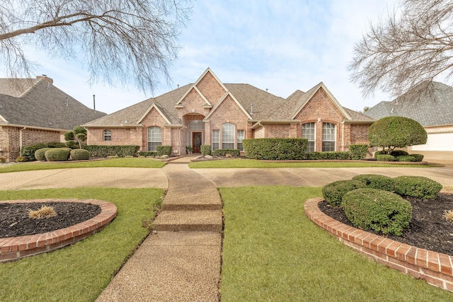 french provincial home featuring brick siding, a front yard, and a shingled roof