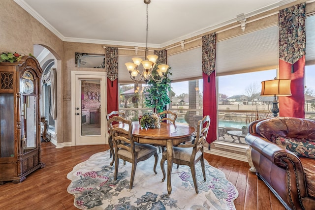 dining space with ornamental molding, arched walkways, wood-type flooring, baseboards, and a chandelier