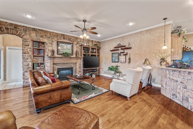 living room with wood finished floors, visible vents, ceiling fan, ornamental molding, and a glass covered fireplace