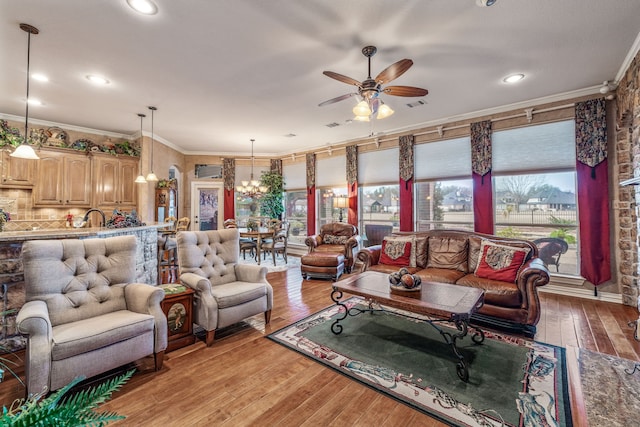 living room with visible vents, ceiling fan with notable chandelier, recessed lighting, light wood-style floors, and crown molding