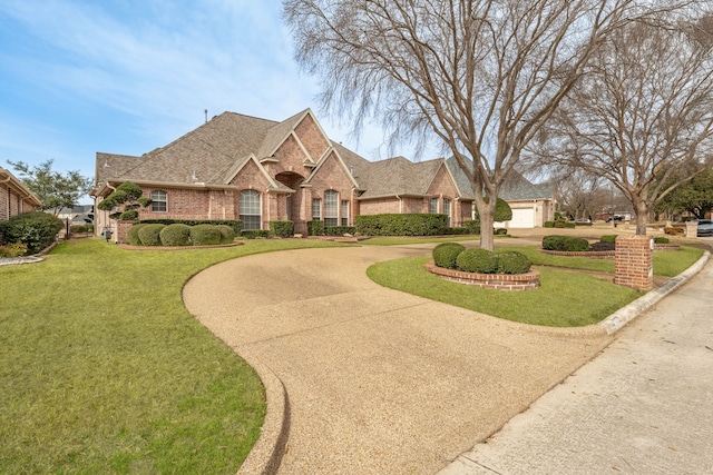 view of front of property featuring a front lawn, curved driveway, brick siding, and a shingled roof