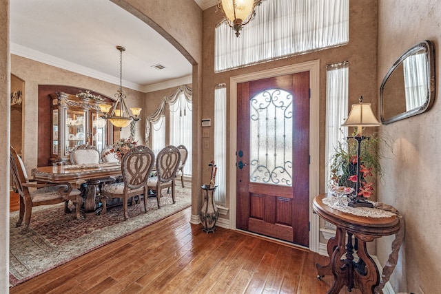 foyer entrance with visible vents, an inviting chandelier, arched walkways, hardwood / wood-style flooring, and crown molding