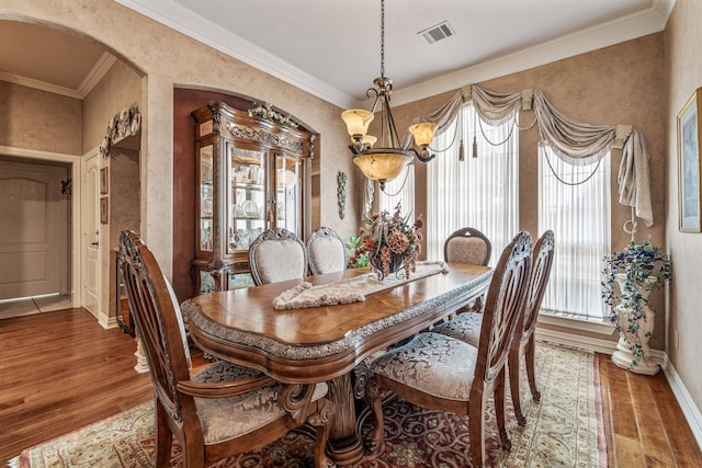 dining room with ornamental molding, wood finished floors, visible vents, and arched walkways