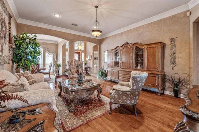 living area with visible vents, light wood-style flooring, ornamental molding, arched walkways, and baseboards