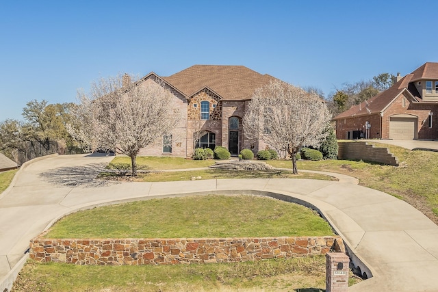 french provincial home with a garage, brick siding, concrete driveway, and a front lawn