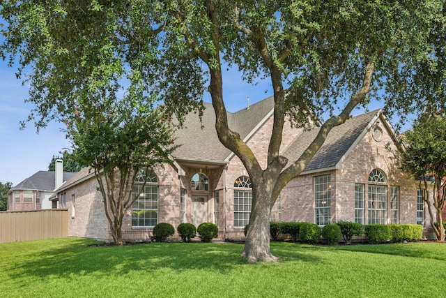 view of front of home with brick siding, a shingled roof, a front yard, and fence