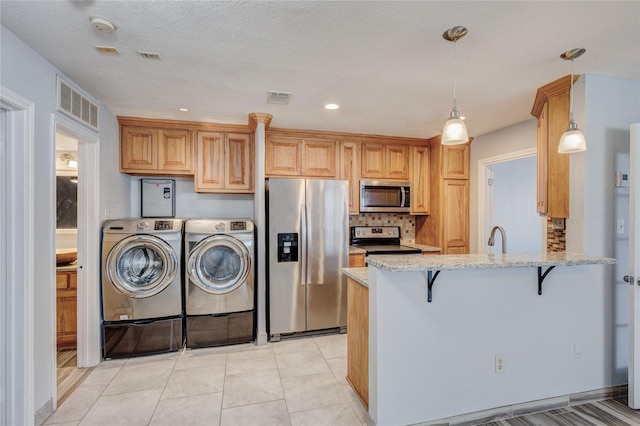 kitchen featuring washing machine and clothes dryer, visible vents, appliances with stainless steel finishes, and light stone countertops