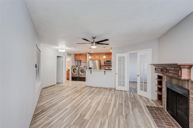 unfurnished living room featuring washing machine and clothes dryer, light wood finished floors, ceiling fan, a fireplace, and french doors