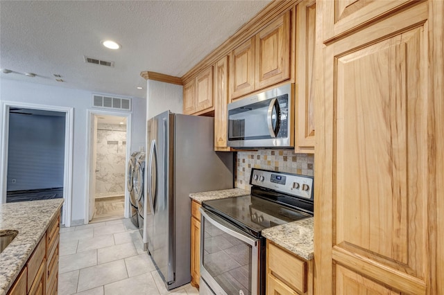 kitchen with washing machine and clothes dryer, light stone counters, visible vents, and stainless steel appliances