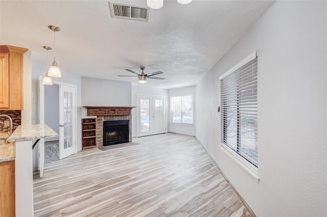 living room with visible vents, light wood-style floors, a fireplace, and french doors