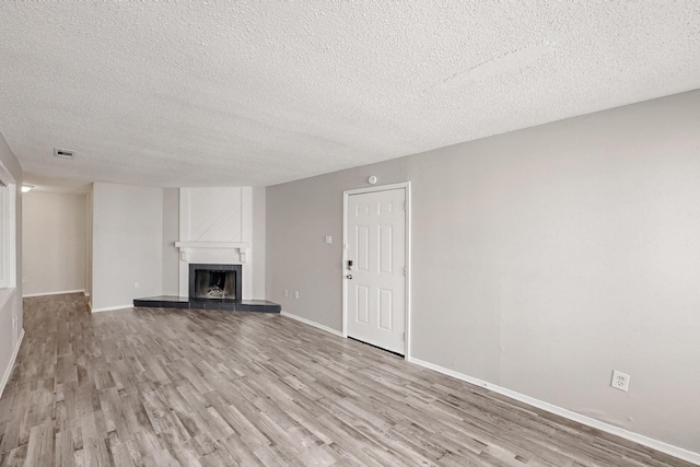 unfurnished living room with visible vents, a textured ceiling, wood finished floors, a fireplace, and baseboards