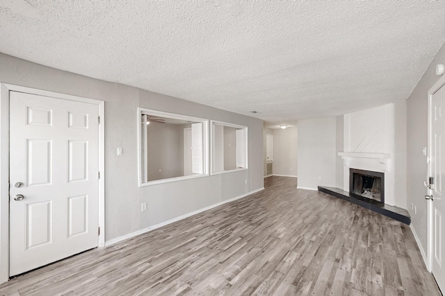 unfurnished living room with wood finished floors, a fireplace with raised hearth, and baseboards