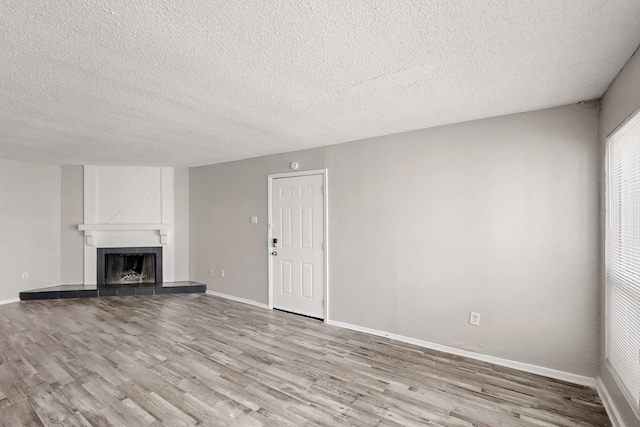 unfurnished living room featuring a fireplace, a textured ceiling, baseboards, and wood finished floors