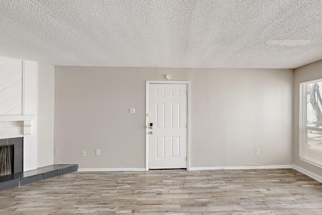 unfurnished living room featuring baseboards, a textured ceiling, wood finished floors, and a fireplace