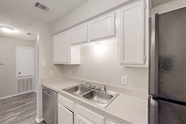 kitchen featuring visible vents, a sink, a textured ceiling, freestanding refrigerator, and dishwasher