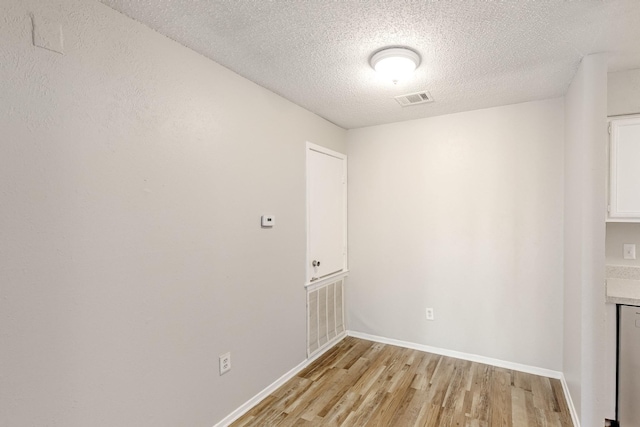 empty room featuring visible vents, baseboards, a textured ceiling, and light wood-style flooring