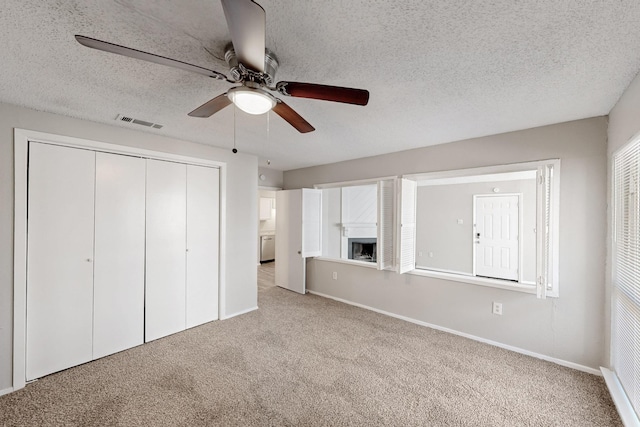 unfurnished bedroom featuring visible vents, a textured ceiling, a closet, carpet floors, and a fireplace