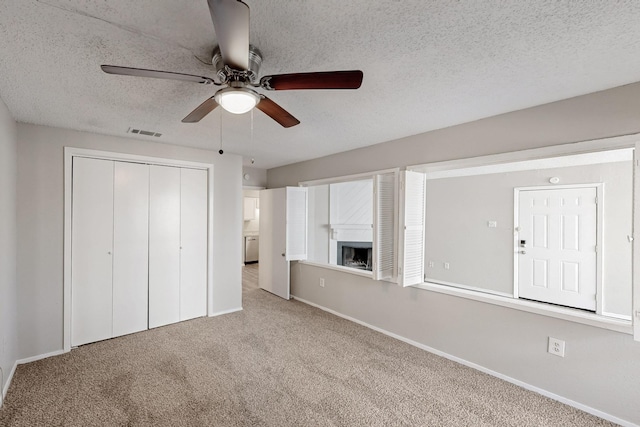 unfurnished bedroom with visible vents, a textured ceiling, a closet, carpet, and a fireplace