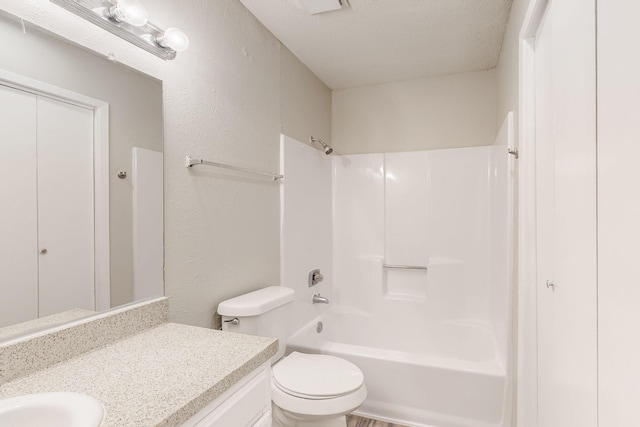 bathroom with toilet, washtub / shower combination, vanity, and a textured wall