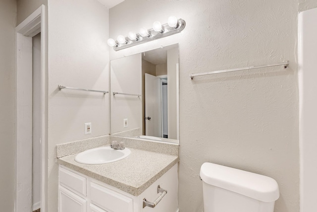 bathroom featuring toilet, vanity, and a textured wall