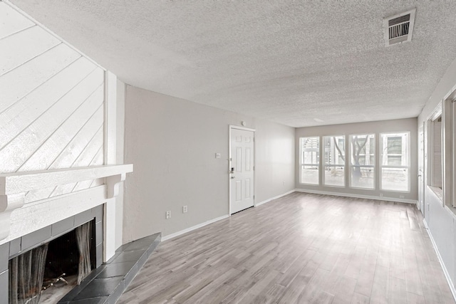 unfurnished living room featuring visible vents, baseboards, a fireplace, wood finished floors, and a textured ceiling