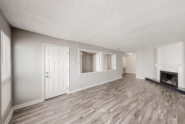 unfurnished living room with wood finished floors, a fireplace with raised hearth, baseboards, and a textured ceiling