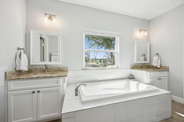 full bath featuring a garden tub, two vanities, and a sink