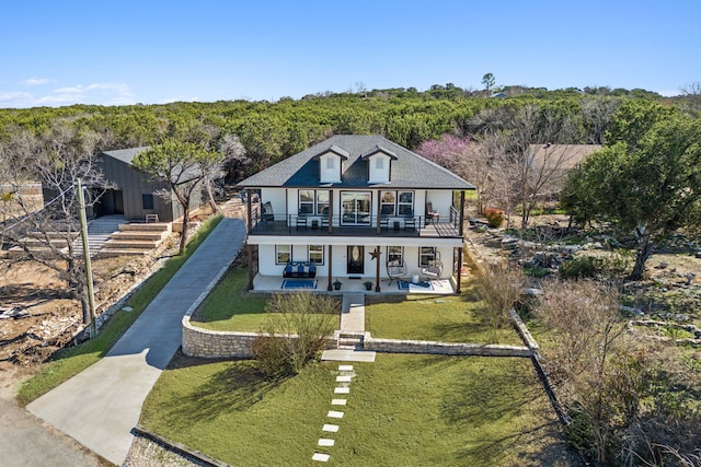 view of front of house with a front lawn, concrete driveway, a patio area, and a view of trees