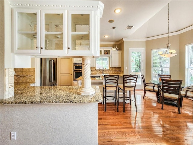 kitchen with visible vents, light stone countertops, ornamental molding, appliances with stainless steel finishes, and a peninsula