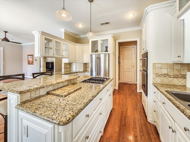 kitchen featuring ornamental molding, decorative backsplash, appliances with stainless steel finishes, a kitchen breakfast bar, and wood finished floors