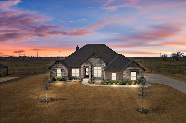 french country style house with stone siding, a rural view, and fence