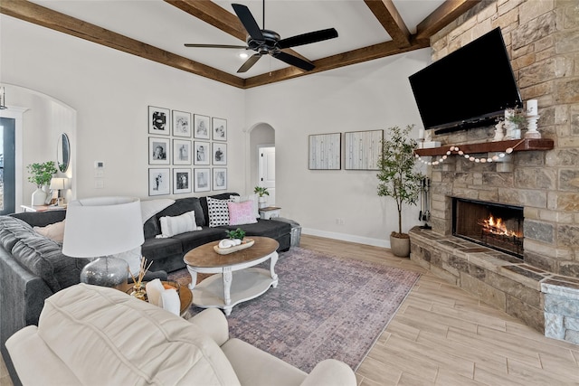 living room featuring beam ceiling, wood finished floors, arched walkways, a fireplace, and baseboards