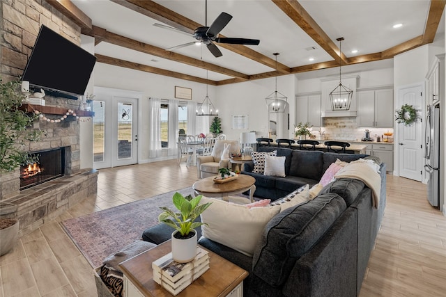 living area featuring beamed ceiling, ceiling fan with notable chandelier, a fireplace, and light wood-style flooring