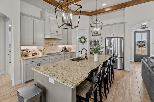 kitchen with arched walkways, a sink, decorative backsplash, black electric stovetop, and stainless steel fridge