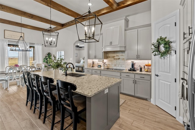 kitchen featuring light stone counters, a kitchen island with sink, a sink, a kitchen bar, and backsplash