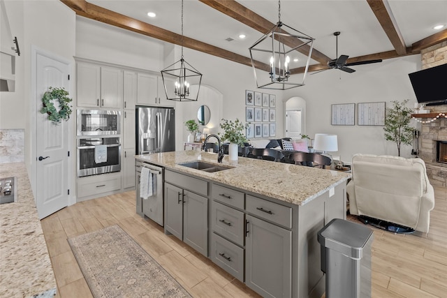 kitchen with gray cabinetry, a sink, open floor plan, stainless steel appliances, and a stone fireplace