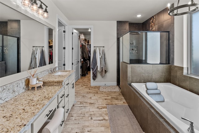 full bath featuring vanity, baseboards, a stall shower, a spacious closet, and a garden tub