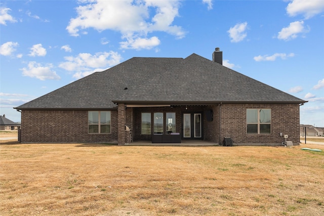 rear view of house with a patio area, a lawn, a shingled roof, and brick siding