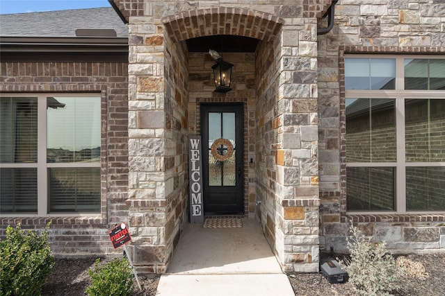 property entrance featuring stone siding and a shingled roof