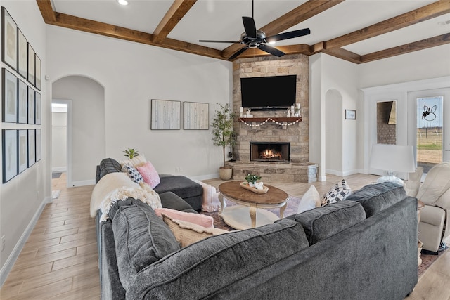 living area featuring light wood-style floors, a fireplace, arched walkways, and baseboards