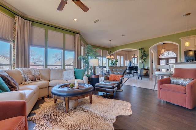 living room with visible vents, ornamental molding, ceiling fan with notable chandelier, wood finished floors, and arched walkways