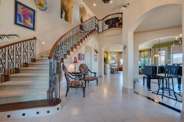 stairway featuring tile patterned flooring, crown molding, baseboards, an inviting chandelier, and a towering ceiling