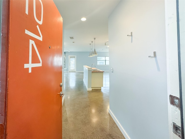 hallway featuring visible vents, a sink, recessed lighting, baseboards, and concrete flooring