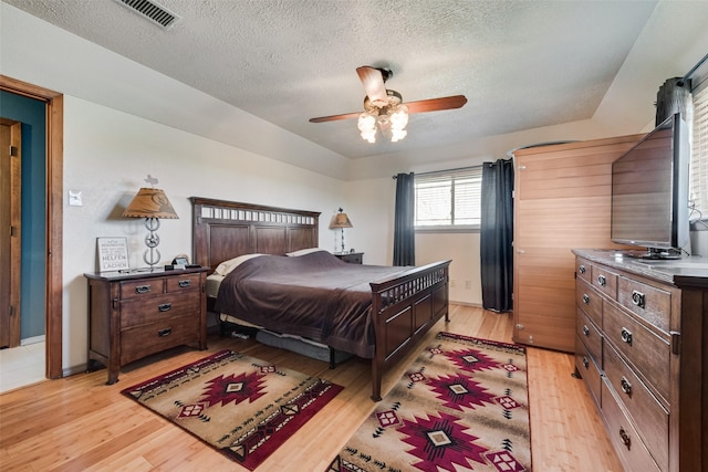 bedroom featuring ceiling fan, visible vents, a textured ceiling, and light wood-style flooring