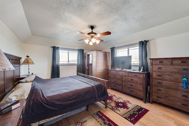 bedroom featuring multiple windows, light wood-style floors, ceiling fan, and a textured ceiling