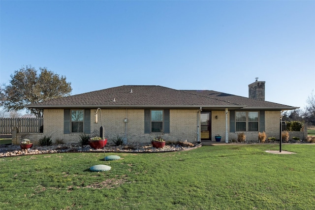 view of front of house with brick siding, a chimney, a front yard, and fence