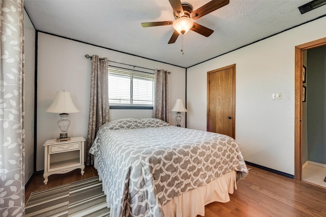 bedroom featuring wood finished floors, baseboards, visible vents, ceiling fan, and a textured ceiling